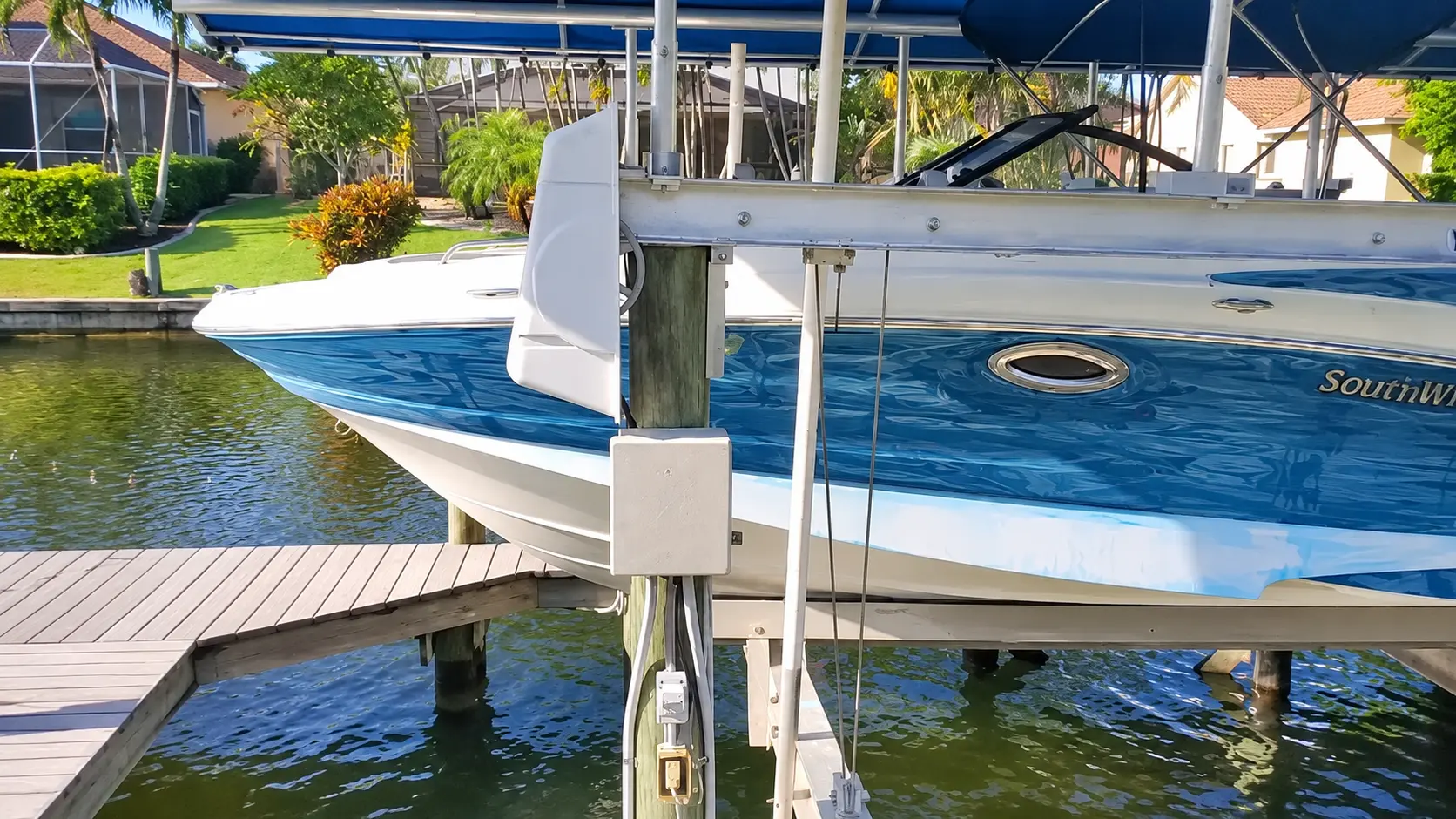 Blue and white boat docked at wooden pier with waterfront homes and palm trees in background