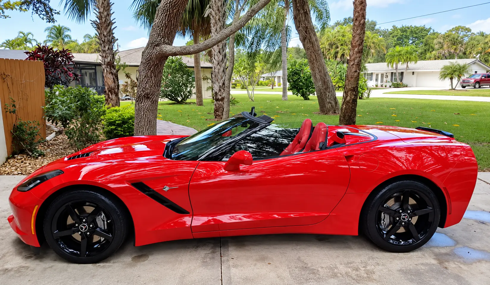 Bright red convertible sports car with retractable black top parked in residential driveway